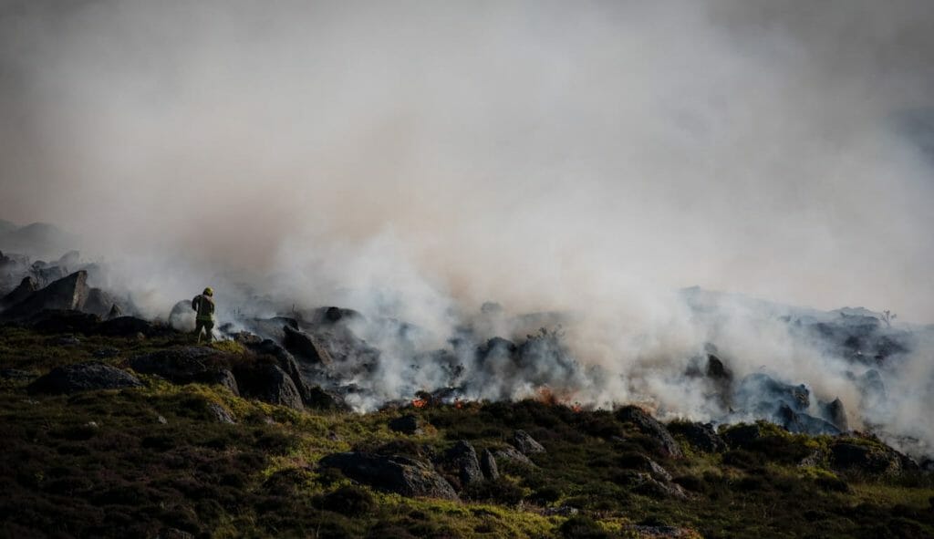 A wildfire smolder on a landscape as firefighters try to put it out.
