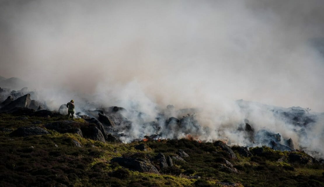 Um incêndio florestal arde numa paisagem enquanto os bombeiros tentam apagá-lo.