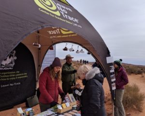 Des personnes discutent avec des coéquipiers de Leave No Trace sous une tente Leave No Trace lors d'un événement extérieur.