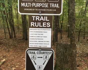 A post at a trailhead has signs indicating what users can use the trail, what the trail rules are, and shows who should yield to who.