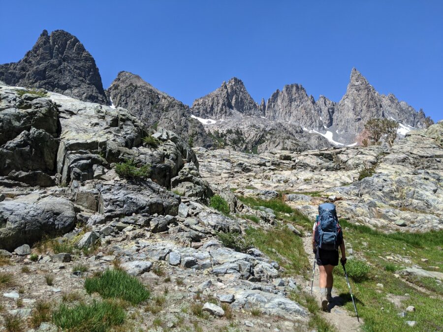 Backpacker on a trail below mountain peaks.