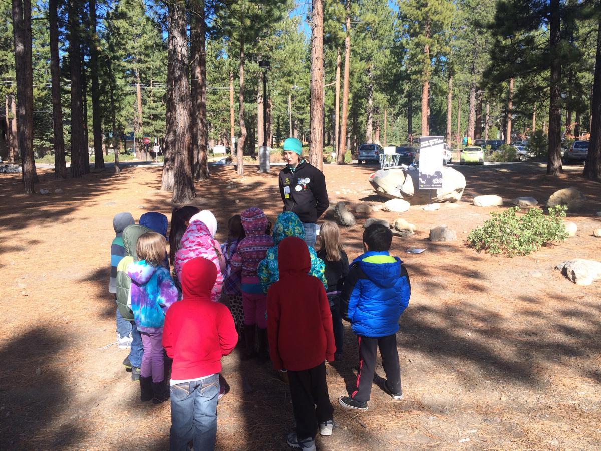 An educator standing in the forest, surrounded by a class of children, teaching the 7 Principles of Leave No Trace